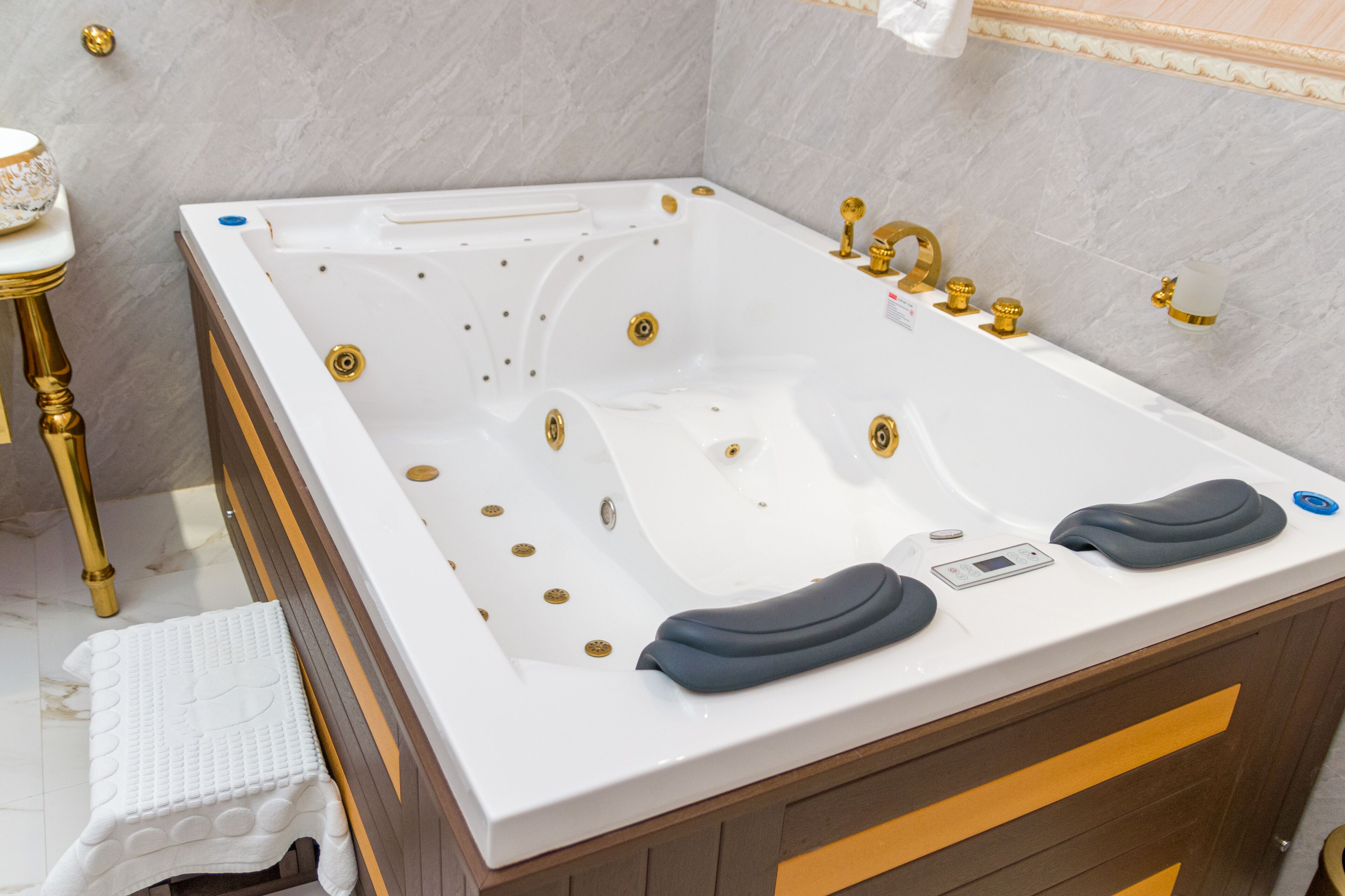 A modern bathroom with a large white bathtub, gold fixtures, and a wooden vanity.