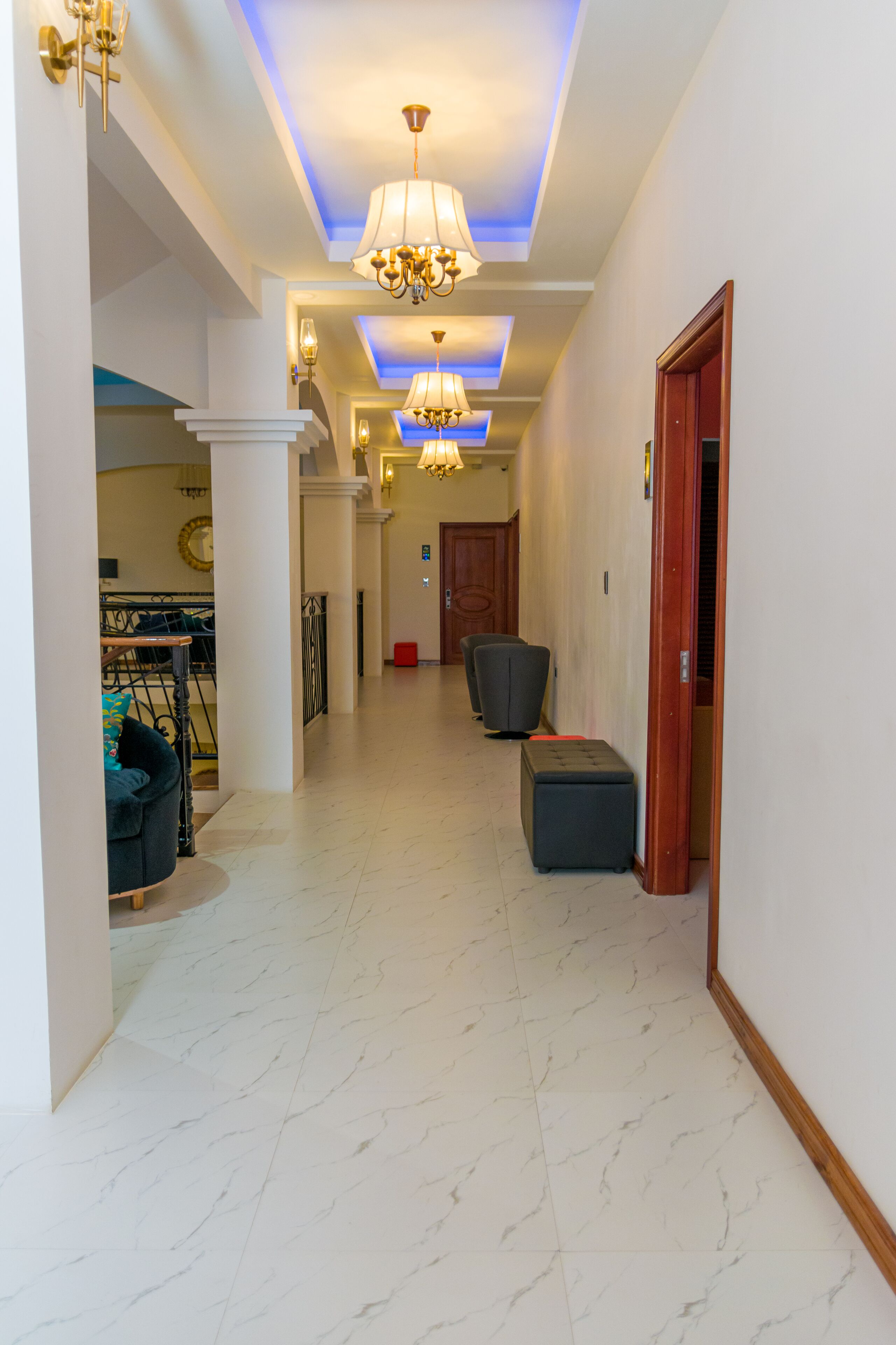 Un pasillo de hotel con piso de mármol, un candelabro y una escalera que lleva a un balcón.