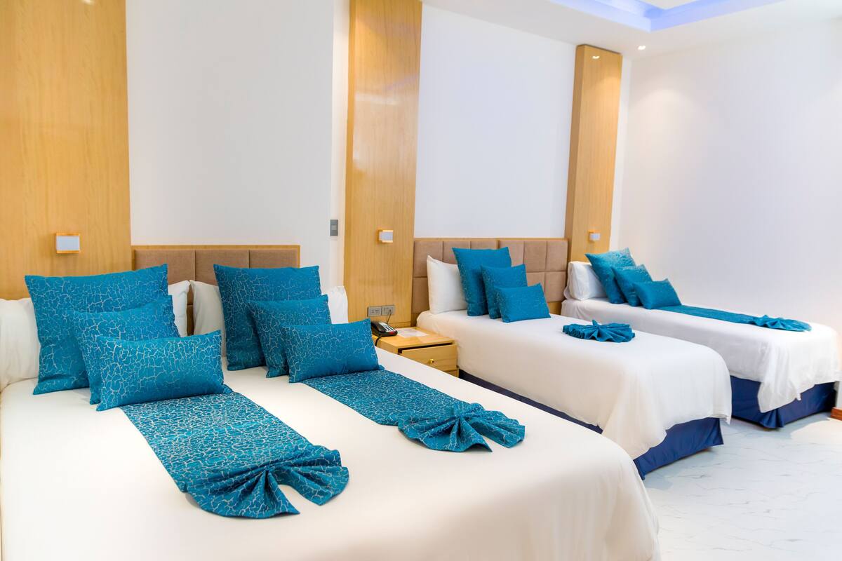 Habitación de hotel con dos camas, cada una con ropa de cama y almohadas azules, un cabecero de madera y una mesita de noche con lámpara.