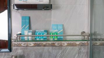 A bathroom with a marble wall, a glass shelf with toiletries, a sink, and a mirror.
