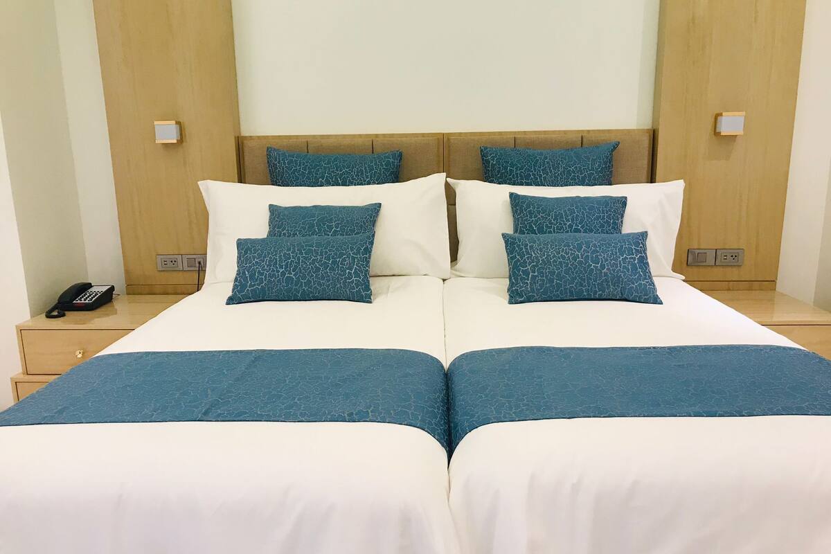 Una cama doble con ropa de cama blanca y azul, dos mesitas de noche y un teléfono en una de ellas.