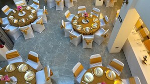 A hotel lobby with multiple round tables, each surrounded by white chairs with gold sashes. - L'ver Hotel (Somoto)