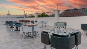 A rooftop terrace with outdoor seating, including round tables and chairs, under a sunset sky. - L'ver Hotel (Somoto)