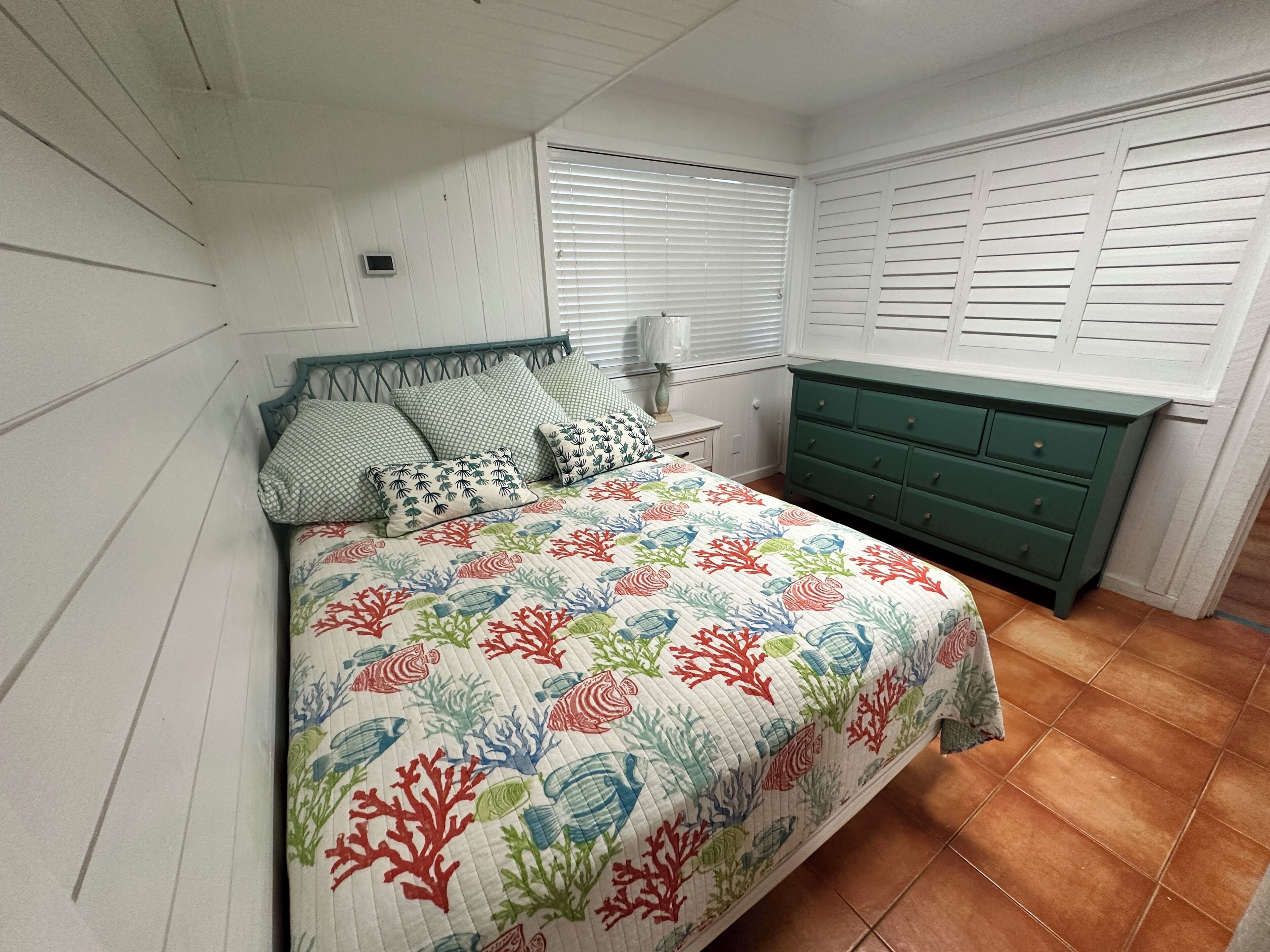 A bedroom with a bed, a nightstand, a dresser, and a window with blinds.