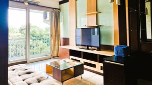 Una sala de estar moderna con una mesa de centro de vidrio, un sofá, un televisor de pantalla plana y un balcón con vistas a zonas verdes.
