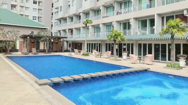 Una piscina con sillas de descanso y un edificio con balcones al fondo.