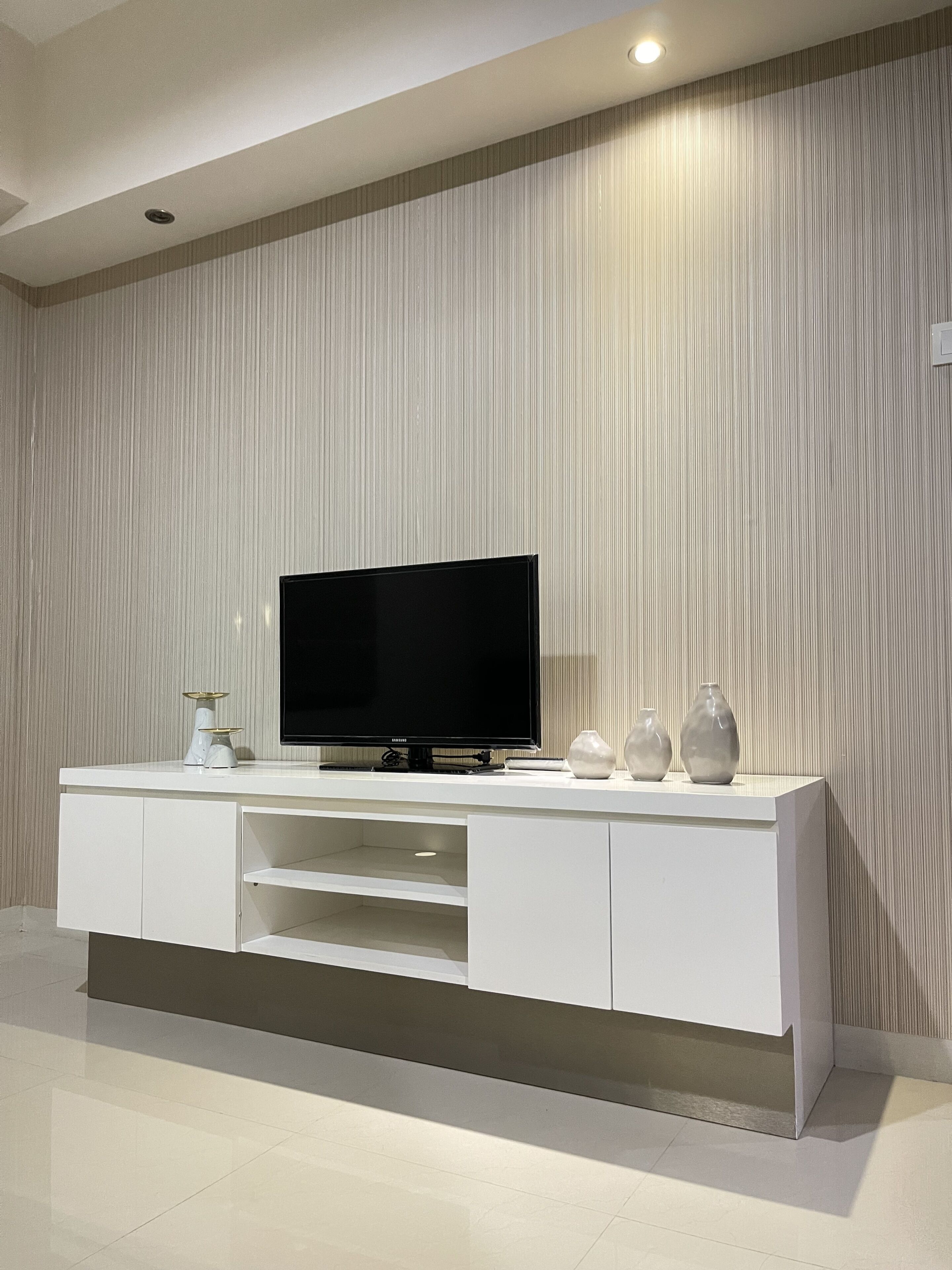 Een moderne woonkamer met een flatscreen televisie op een witte tv-meubel, een structuurwand en een strak, minimalistisch design.