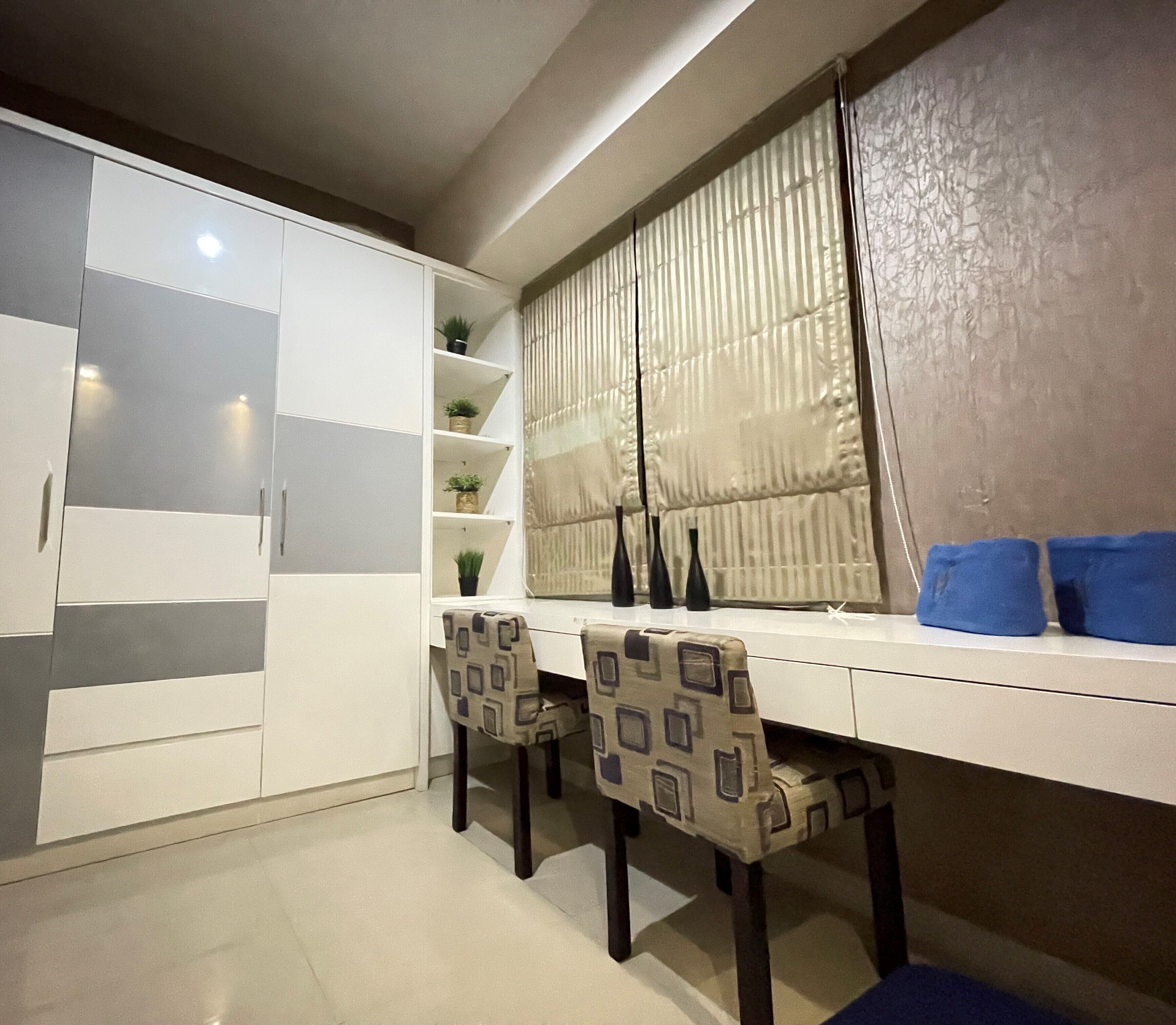A modern kitchen with white cabinets, a dining table, two chairs, and a window with blinds.
