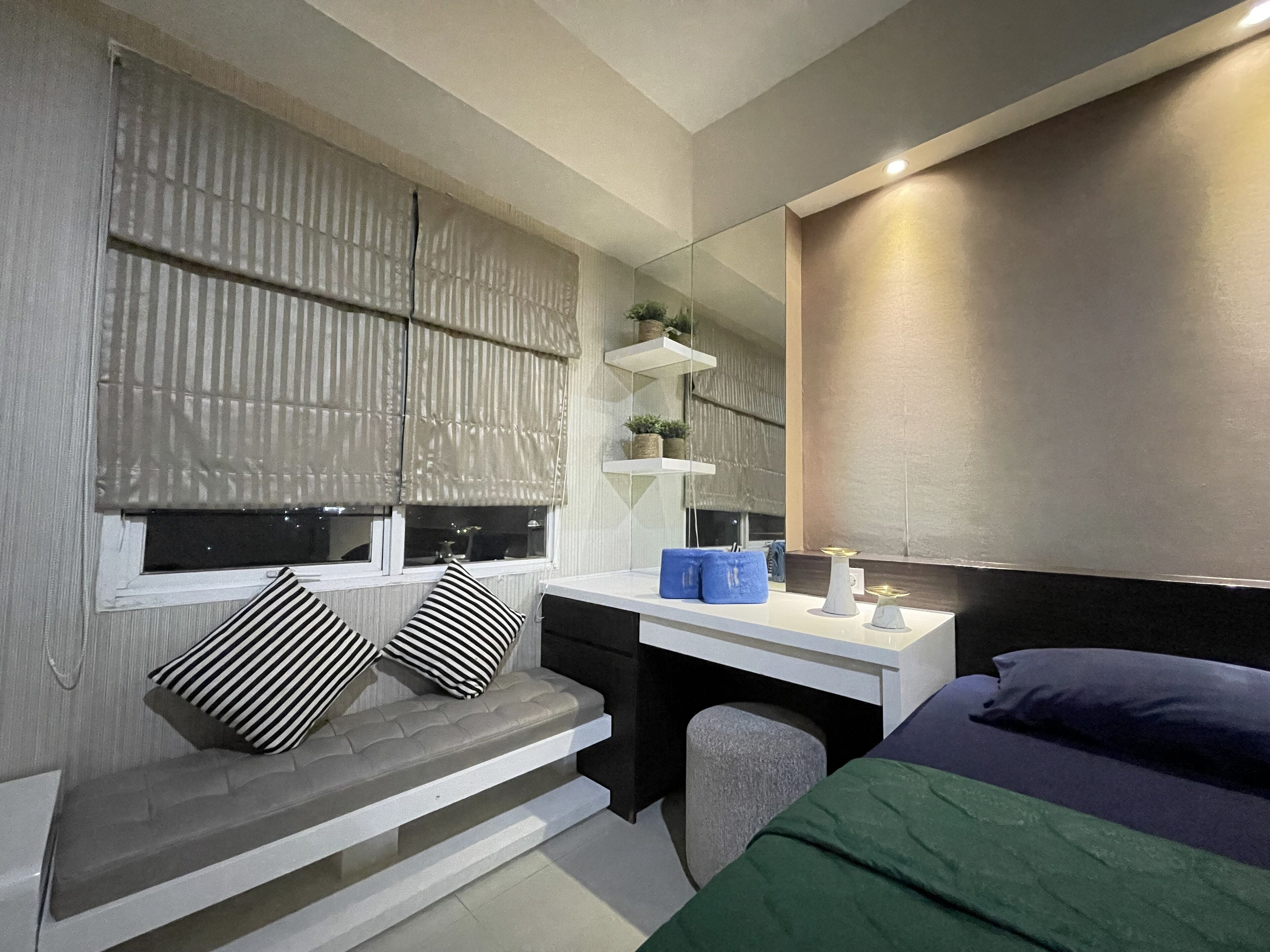 A bedroom with a bed, a desk, a chair, a window with blinds, and a mirror.