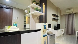 Una cocina moderna con encimera negra, armarios blancos, microondas integrado y un refrigerador pequeño.