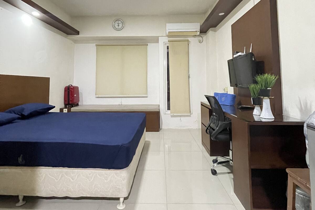 Een hotelkamer met een bed, bureau, stoel, televisie en een kleine plant.