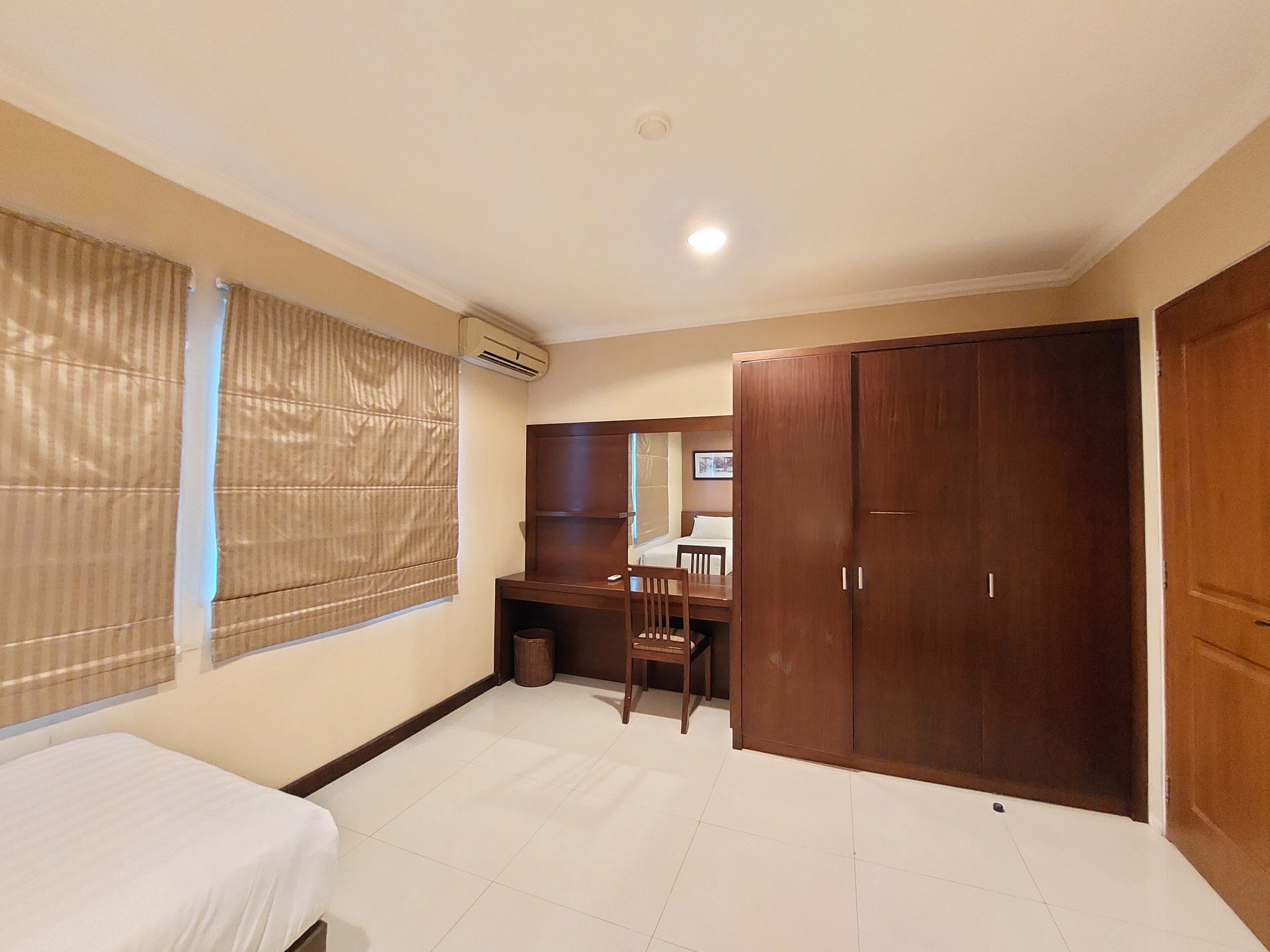 Un dormitorio con cama, escritorio, silla, armario y ventana con persianas.