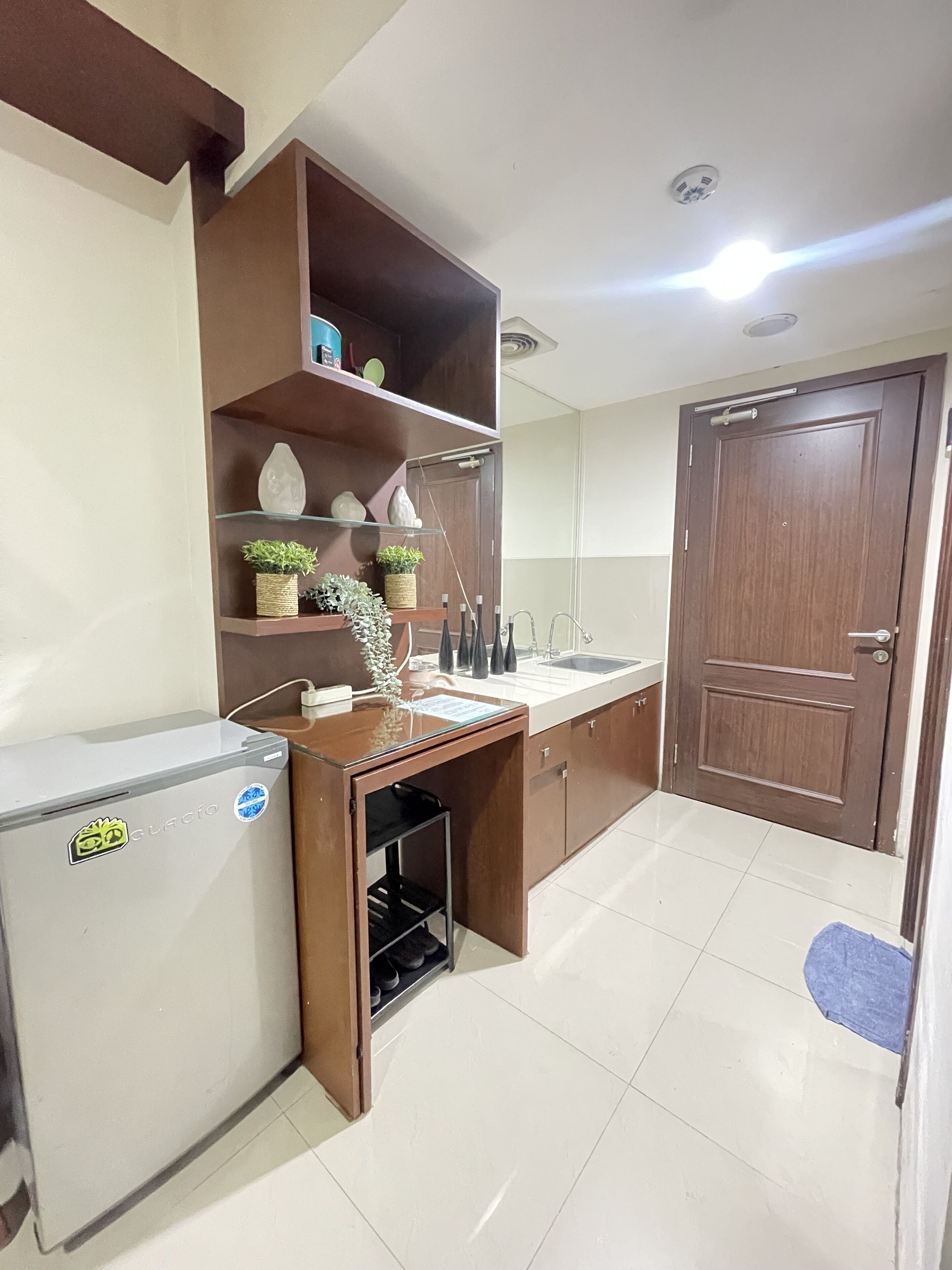 A compact kitchen with a refrigerator, a sink, and wooden shelves.