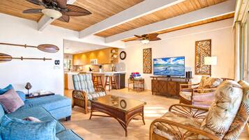 A spacious living area with a sofa, chairs, a coffee table, a TV, and a kitchen in the background.