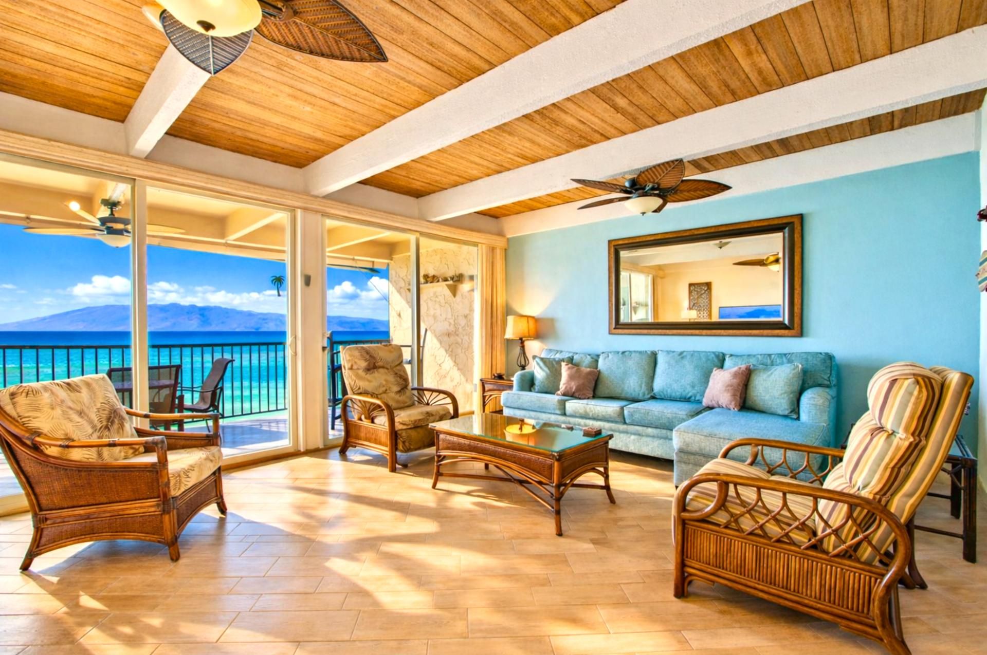 A spacious living area with wicker furniture, a blue sofa, and a large window offering a view of the ocean.