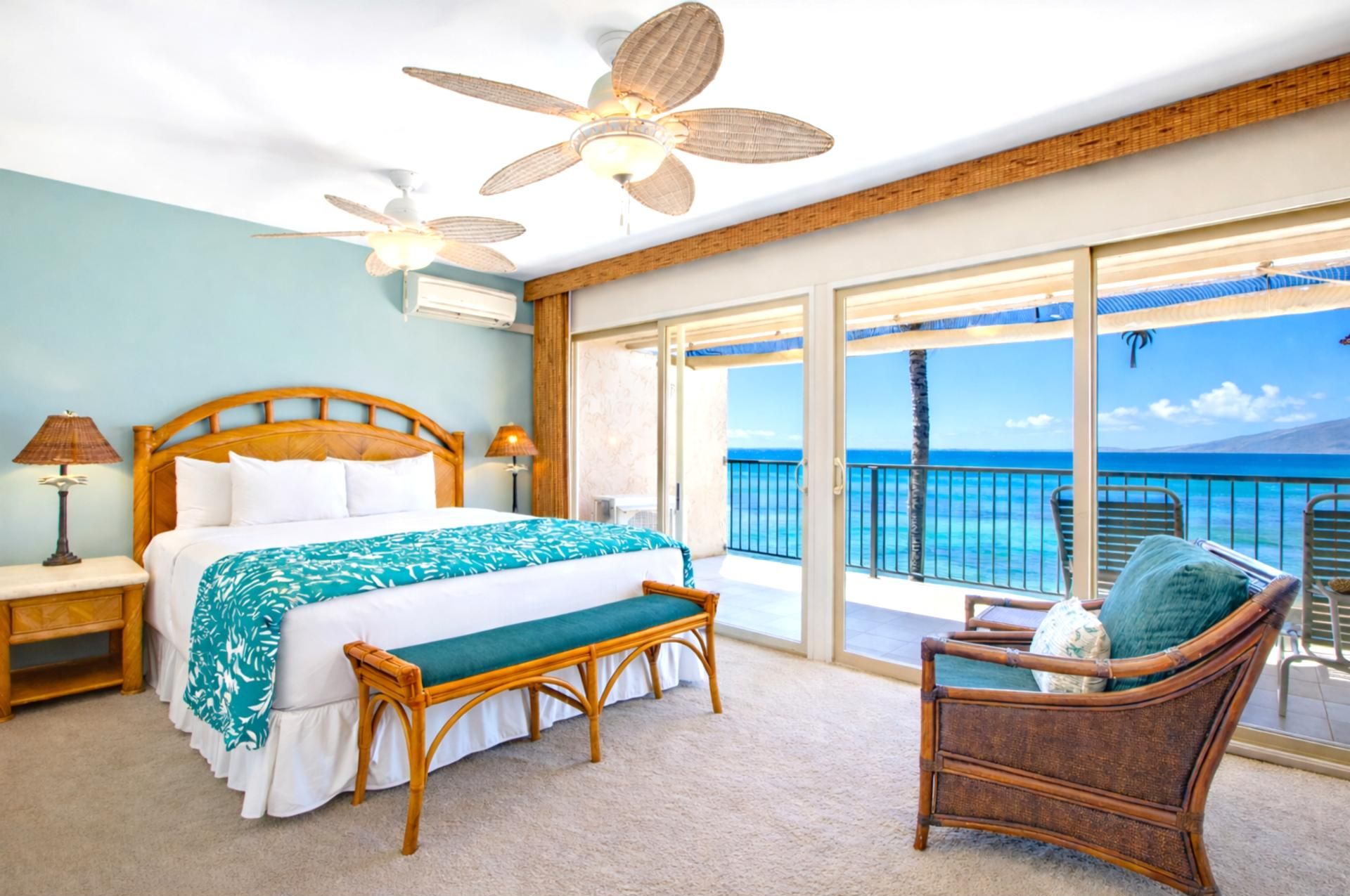 A bedroom with a bed, a bench, a chair, and a balcony with a view of the ocean.