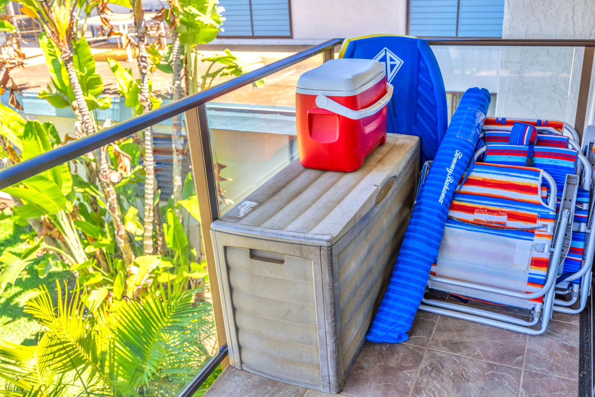 Un balcón con un refrigerador pequeño, una silla azul y un cojín a rayas.