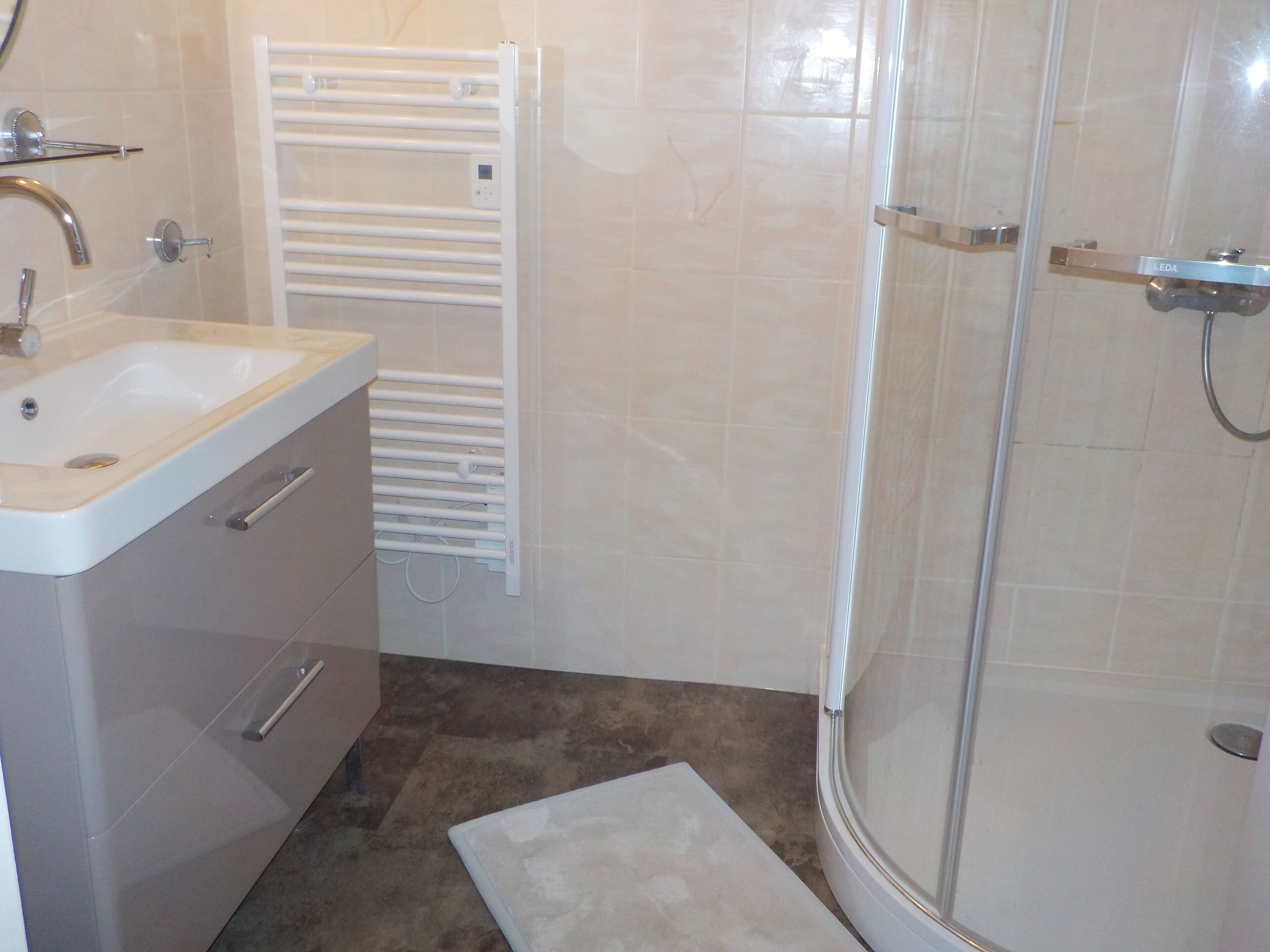 A bathroom with a sink, mirror, towel rack, and a shower enclosure.