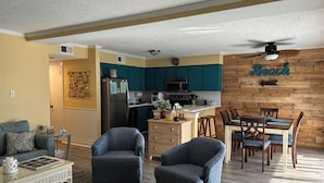 A modern kitchen with teal cabinets, a dining area with wooden chairs, and a living room with a sofa and armchairs. - Experience North Ocean City near the sandy shores (Ocean City)