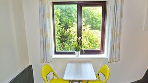 A room with a window, a table, and two yellow chairs. - Station 1 Bed Apartment – Stayseekers (Wiltshire)