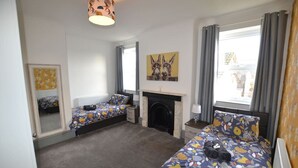 Une chambre avec deux lits, une cheminée et une grande fenêtre avec des rideaux.