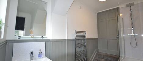 A bathroom with a sink, mirror, towel rack, shower, and a door.