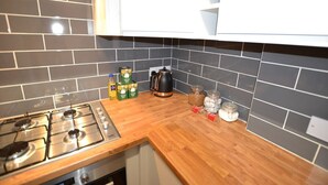 Cozinha com fogão a gás, bancada de madeira e painel de azulejos pretos.