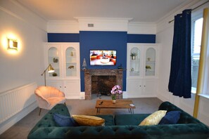 A living room with a fireplace, a television, and a green sofa. - Mayflower 2 bed Boutique Apartment – Stayseekers (Wiltshire)