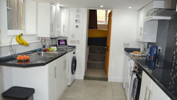 A compact kitchen with white cabinets, a washing machine, a sink, and a trash bin.