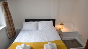 A hotel room with a bed, a nightstand, a lamp, and a window with curtains.