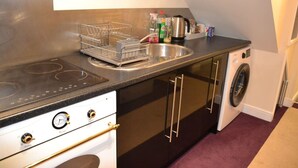 A compact kitchen with a stove, sink, and built-in washing machine. - Olive Tree 2 bed Apartment - Stayseekers (Salisbury)