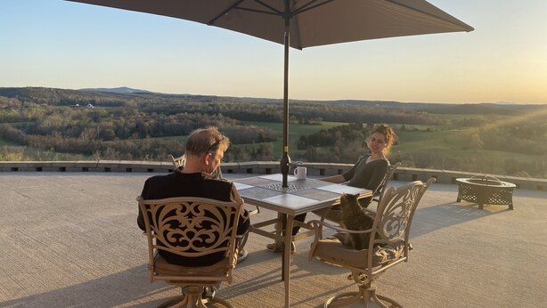 Dos personas sentadas en una mesa al aire libre con una sombrilla grande, con vistas a un paisaje pintoresco.