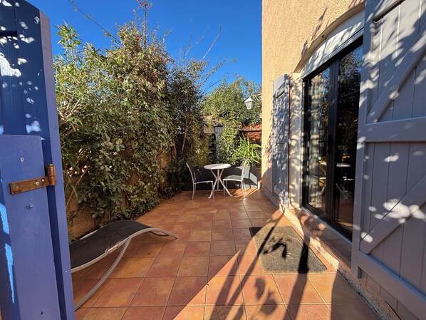 Un patio con mesa y sillas, rodeado de plantas y una puerta.