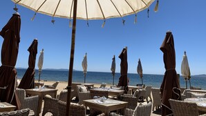Terrasse mit Sonnenschirmen und Korbmöbeln mit Blick auf einen Strand und das Meer.