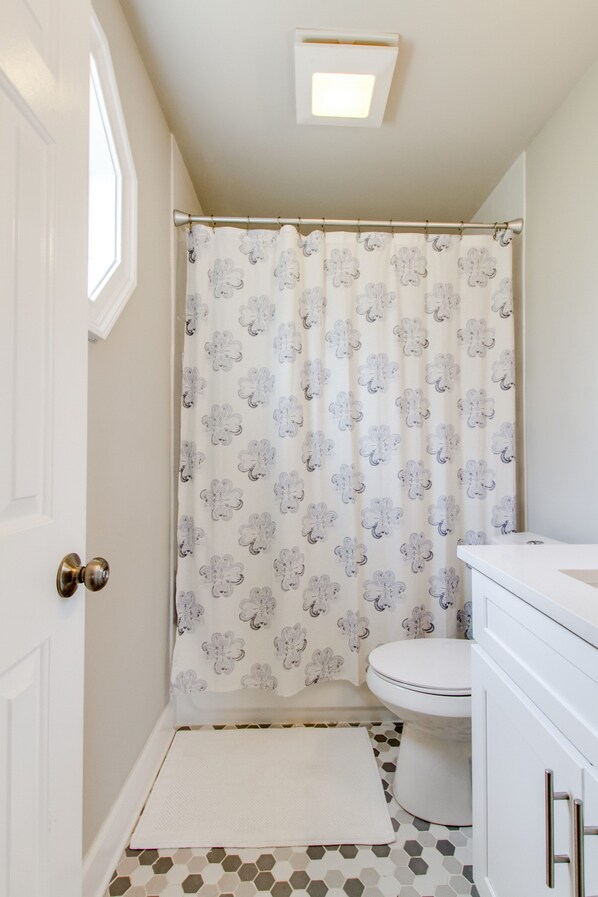Un baño con cortina de ducha, inodoro y armarios blancos.