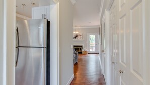 Un couloir avec un réfrigérateur en acier inoxydable, des armoires blanches et un plancher en bois.