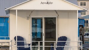 Una struttura galleggiante chiamata Aqua Lodge con una terrazza coperta, due poltrone Adirondack blu e un portafinestra in vetro.