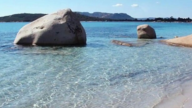 Une plage avec une eau claire et de gros rochers.
