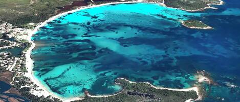 Vista aérea de una zona costera con aguas turquesas cristalinas, playas de arena y vegetación verde exuberante.