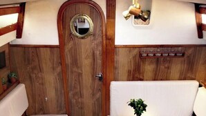 Un intérieur compact aux panneaux de bois, doté d’une porte ronde, d’une petite table ornée d’une plante et de sièges blancs rembourrés.