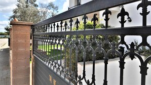 A wrought iron gate with intricate designs, a brick pillar, and a white building with a balcony in the background. - Beautiful spacious holiday home for families with a big swimming pool and garden - Free Wifi (Marratxi)