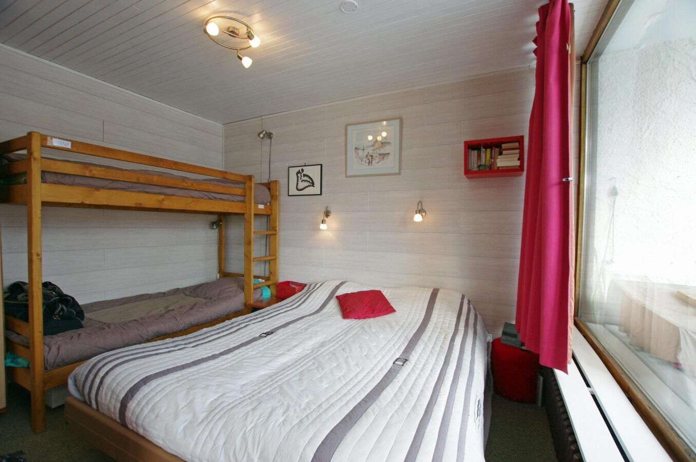 A bunk bed room with a window, a bedside table, and a wall-mounted light fixture.