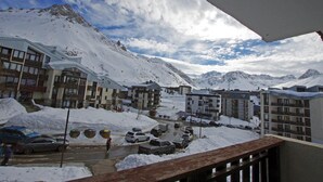 Un pueblo cubierto de nieve con edificios de varios pisos, una calle con coches aparcados y un cielo despejado.