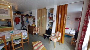 Una habitación pequeña con cama, una mesita, una silla y un rincón de cocina.