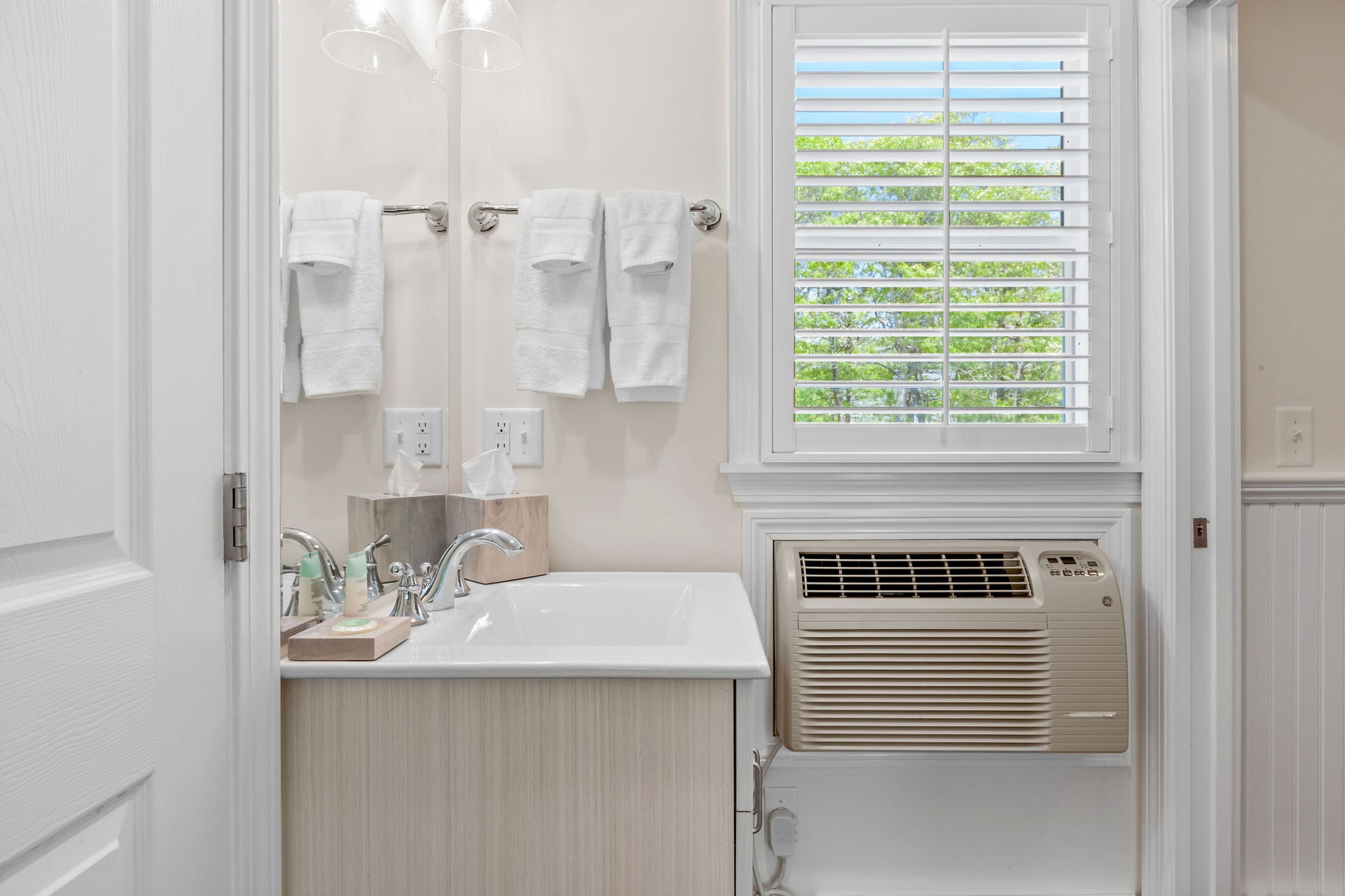 Un baño con lavamanos, toallero, ventana con persianas y un calentador de pared.