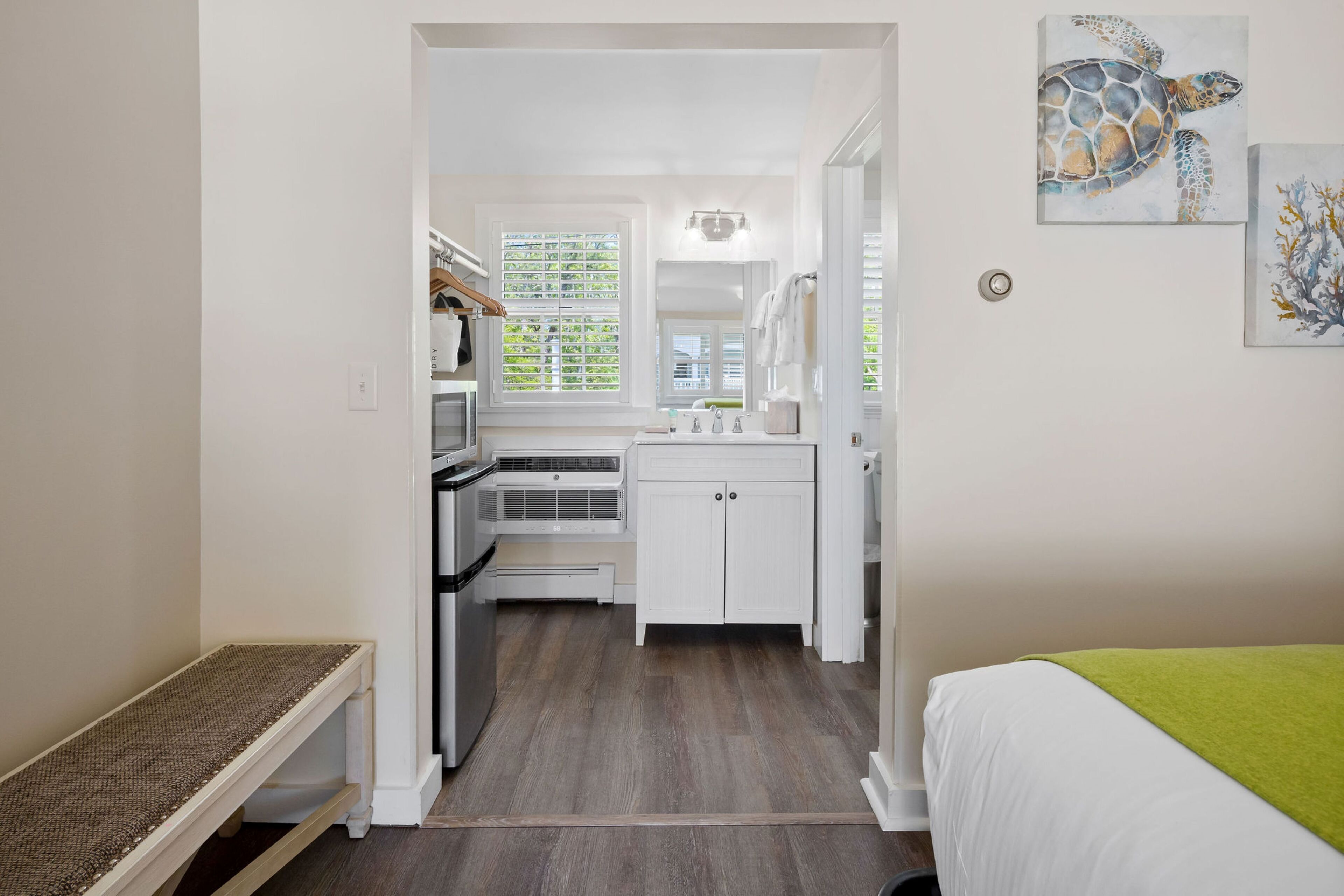 A compact hotel room with a kitchenette, a bed with a green blanket, and artwork on the walls.