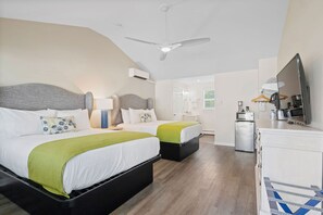 Une chambre d’hôtel moderne équipée de deux lits, d’un ventilateur de plafond, d’une télévision, d’un mini-réfrigérateur et d’une petite kitchenette.