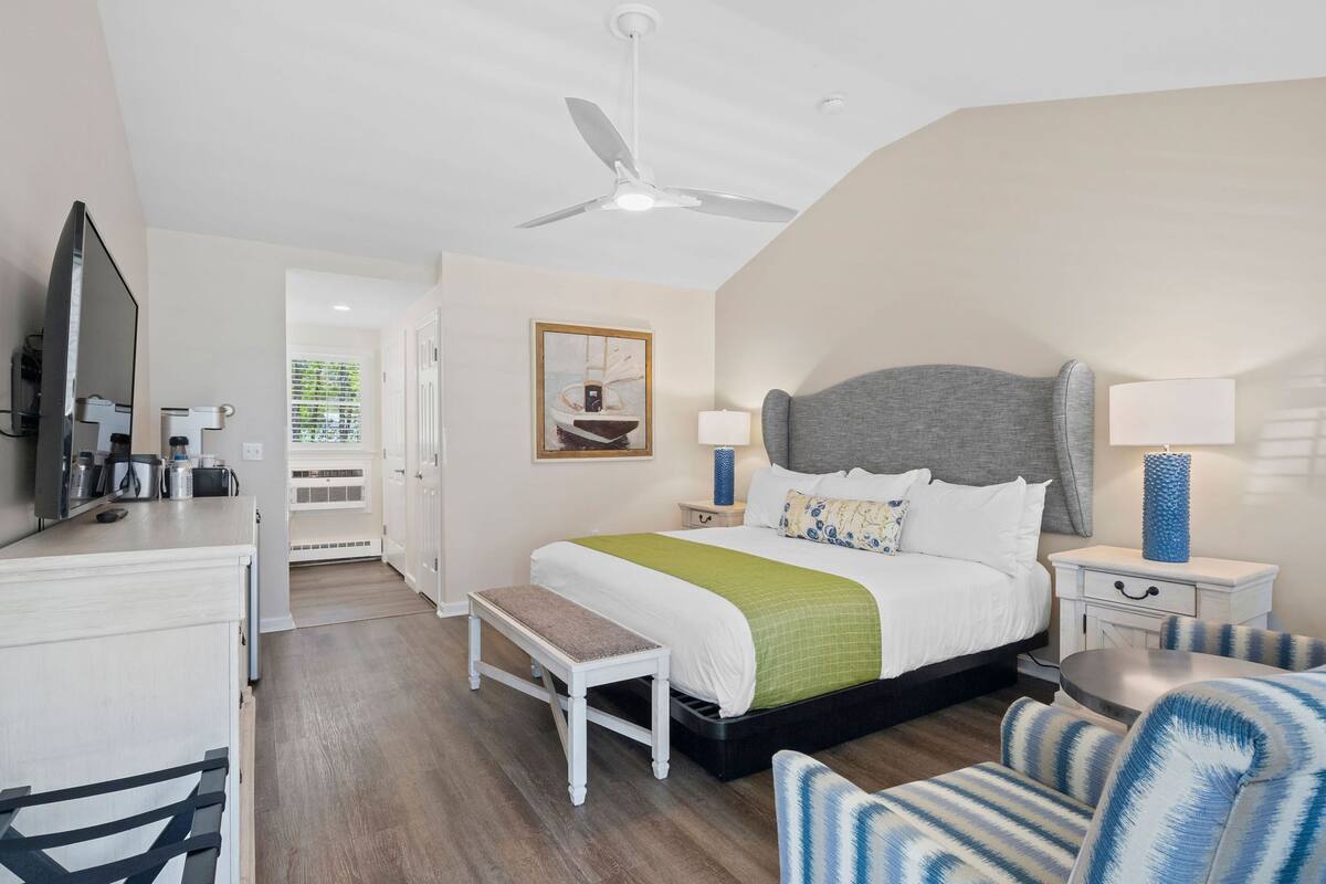 Una habitación de hotel con cama, mesitas de noche, un banco, un televisor y un ventilador de techo.