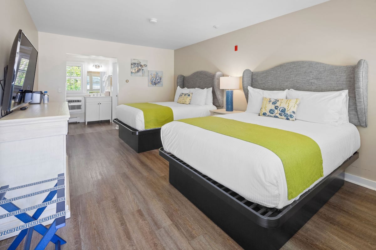 Una habitación de hotel con dos camas, un escritorio, un espejo y una ventana.