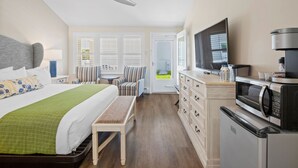 A hotel room with a bed, a bench, a desk, a microwave, and a television. - Pelham on Earle (West Harwich)